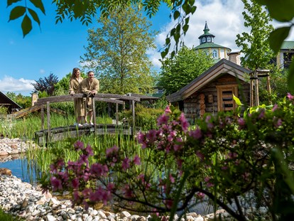 Luxusurlaub - Saunalandschaft: Außensauna - Pärchen auf Brücke im Wellnessgarten - Wellnesshotel Seeschlösschen - Privat-SPA & Naturresort