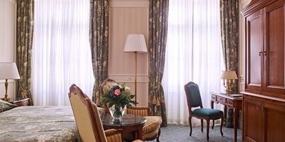 Luxusurlaub - Bettgrößen: King Size Bett - Wien - Die 36 wohnlich gestalteten Deluxe Zimmer verfügen über eine Größe von 35 bis 45 Quadratmeter und sind mit einem großen Doppelbett oder mit 2 getrennten Betten und einer gemütlichen Sitzecke ausgestattet. Die Einrichtung ist elegant, und die Möbel sind mit ausgefallenen Stoffen in den Farben Grün und Gelb bezogen. Die Deluxe Zimmer befinden sich auf unterschiedlichen Stockwerken und bieten teilweise einen Blick auf die Wiener Innenstadt. - Grand Hotel Wien